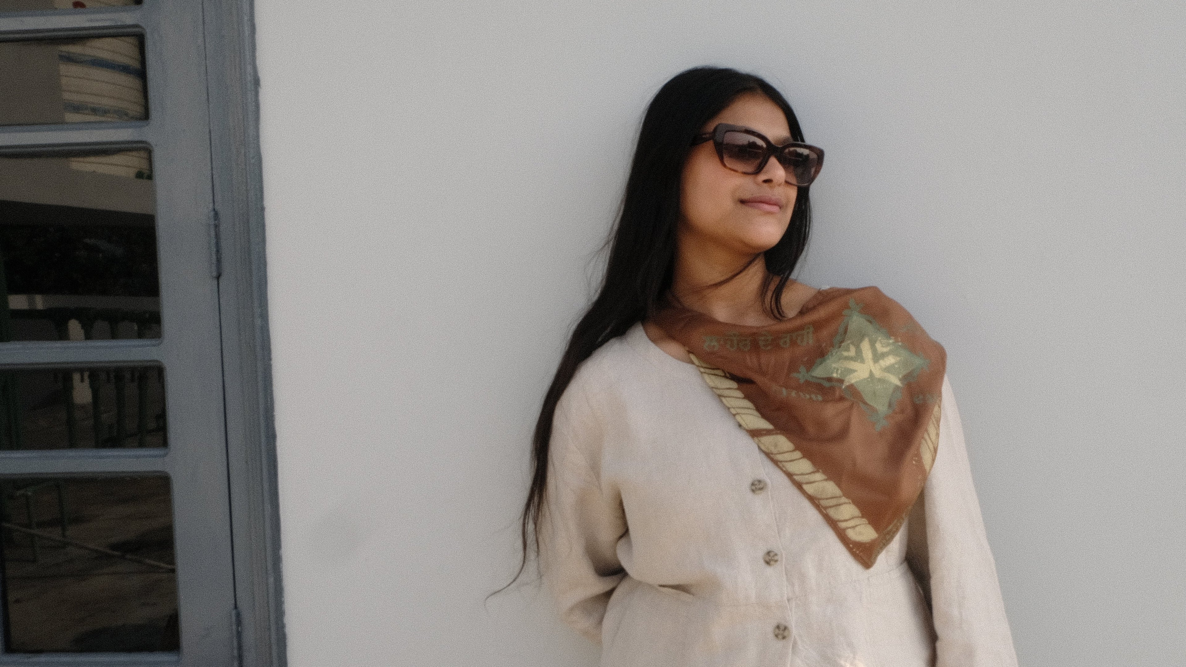 Woman wearing a patterned scarf against a white wall with a window.