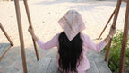 Person wearing a pink shirt and patterned headscarf sitting on a wooden swing.
