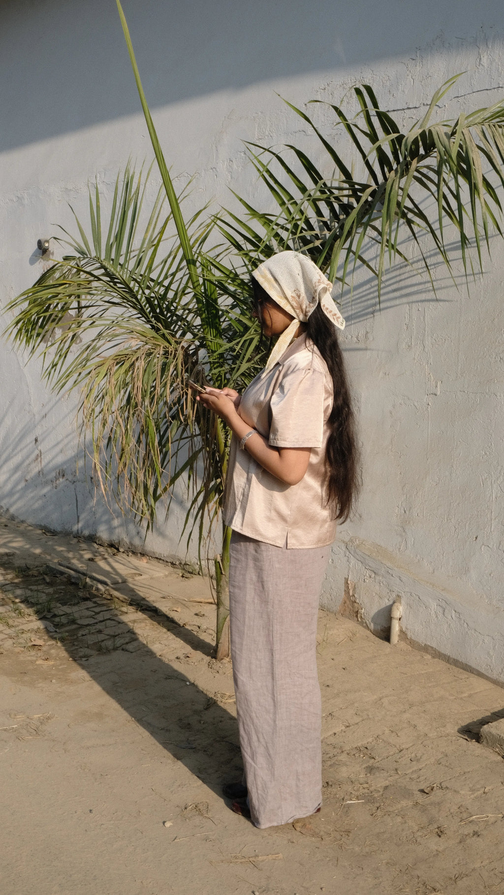 Girl outside looking on her phone in front of a plant