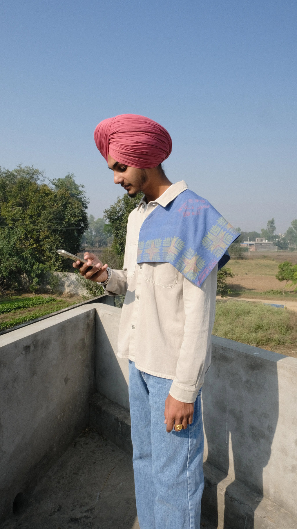 Singh wearing a Denim scarf on his shoulder standing on a concrete surface with a clear sky of Punjab in the background.