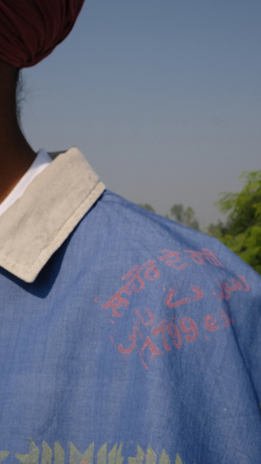 Singh wearing a Denim scarf on his shoulder standing on a concrete surface with a clear sky of Punjab in the background.