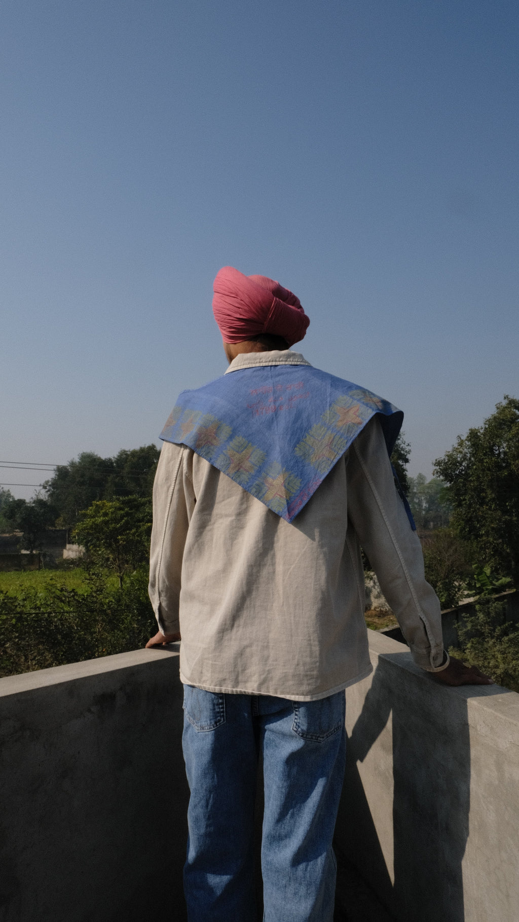 Singh wearing a Denim scarf on his shoulder standing on a concrete surface with a clear sky of Punjab in the background.